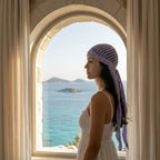 Woman wearing a purple headscarf looking out of an arched window with a scenic view of the sea.Zawjien HeadScarf